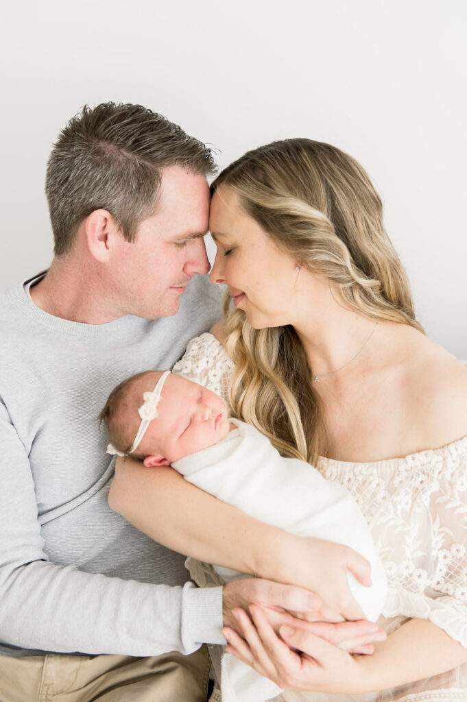 Image of a couple facing each other touching their foreheads together softly, with eyes closed, holding their newborn baby girl, as photographed by Sydney's best maternity photographer Sarah Vassallo Photography