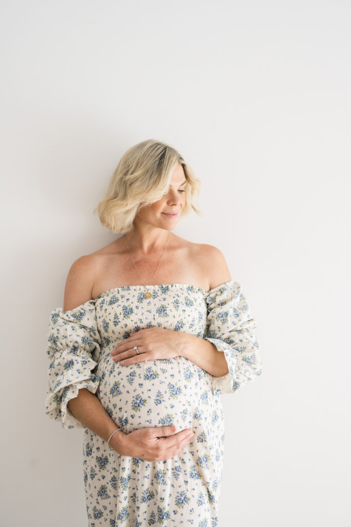 Blonde woman smiling to herself softly while holding her pregnant belly gently as photographed by Sydney Maternity Photographer Sarah Vassallo