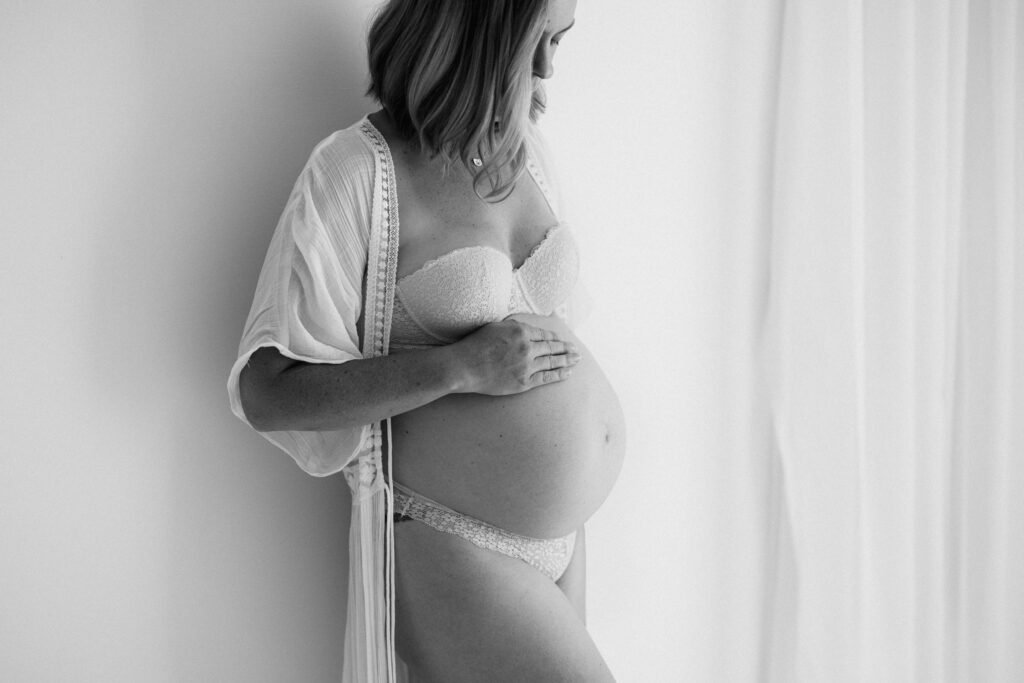 Black and white image of pregnant woman wearing open kimono and looking down at her belly as photographed by Sydney maternity photographer Sarah Vassallo