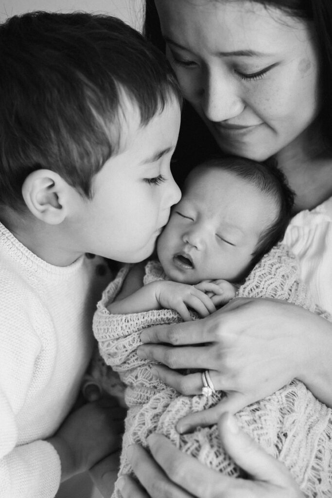 Sydney Newborn photography image of mother holding newborn baby with big brother kissing the baby gently sarah vassallo photography