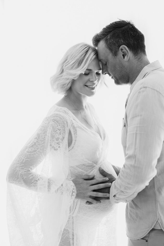 Pregnant mother being embraced by her partner and both smiling sweetly as they await their new baby, photographed in Sydney Pregnancy Photography studio 