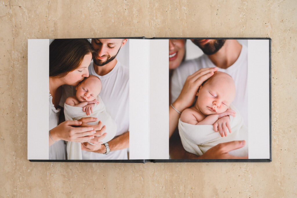 Custom-designed newborn heirloom album opened to a full spread, showcasing storytelling through family portraits and newborn photography