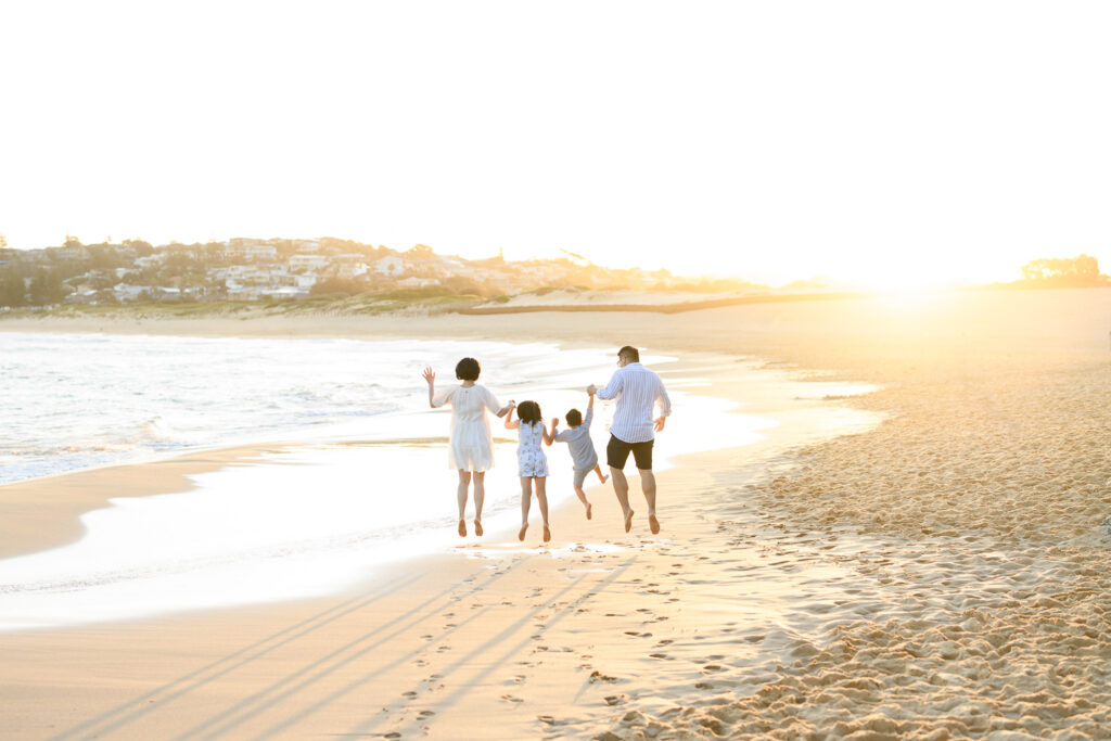 family jumping up in the air on a sunny beach holding hands