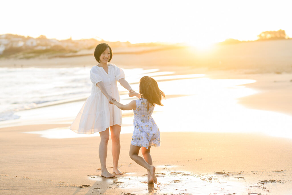 Mother and daughter holding hands and spinning around in the sunshine on a beach