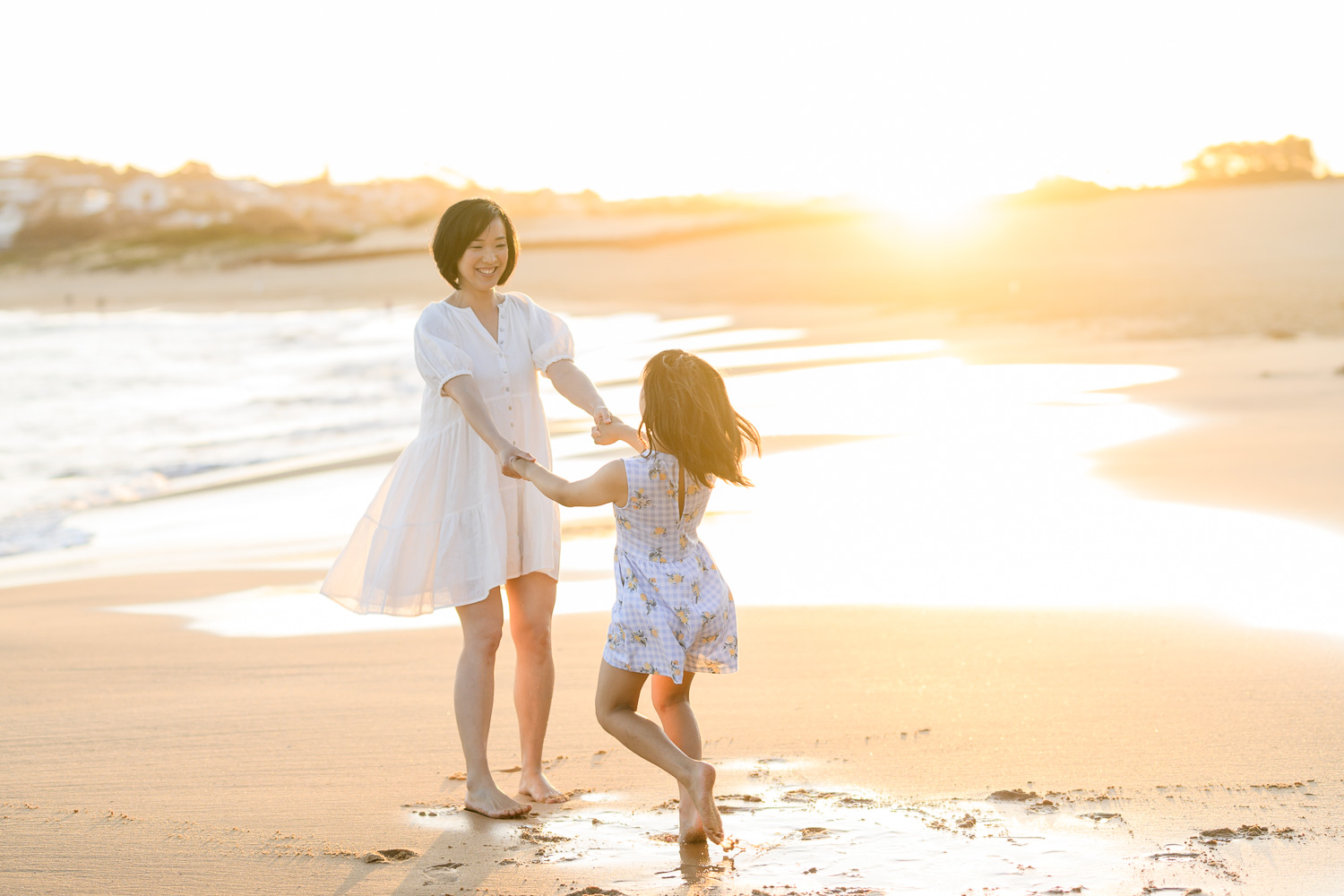 Mother and daughter holding hands and spinning around in the sunshine on a beach