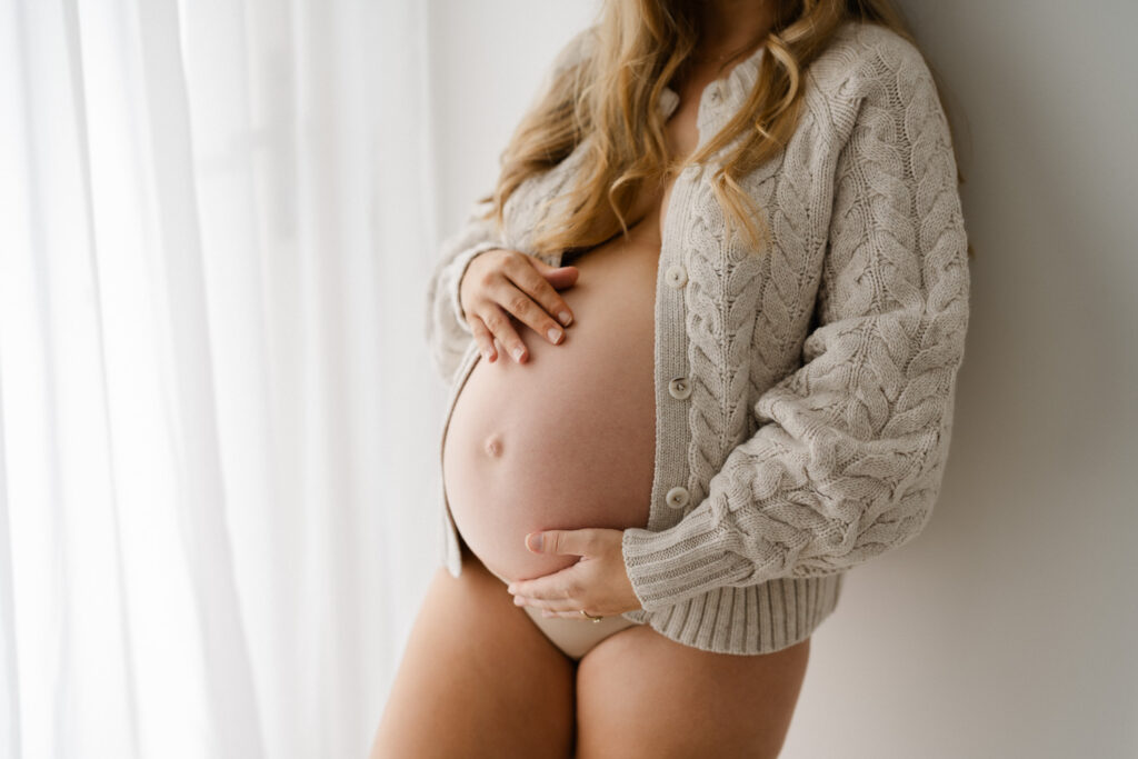 Close-up of baby bump in neutral textured cardigan by DIISH, natural and minimal styling as photographed by minimalist maternity photographer Sarah Vassallo