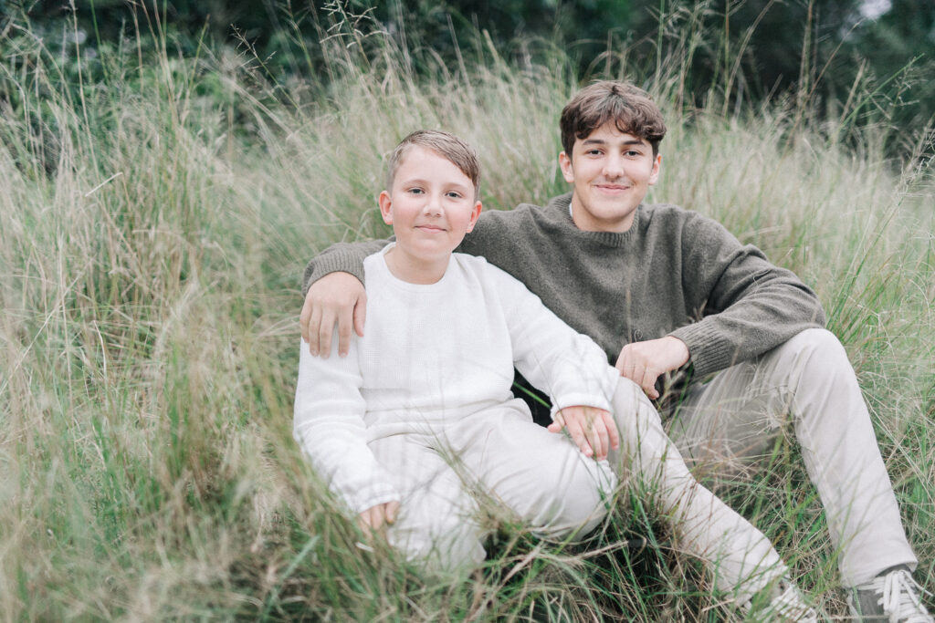 Sydney family photography session – brothers sitting together in long grass smiling sweetly at camera
